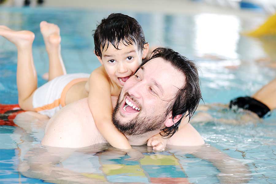 Young boy and father swimming in pool